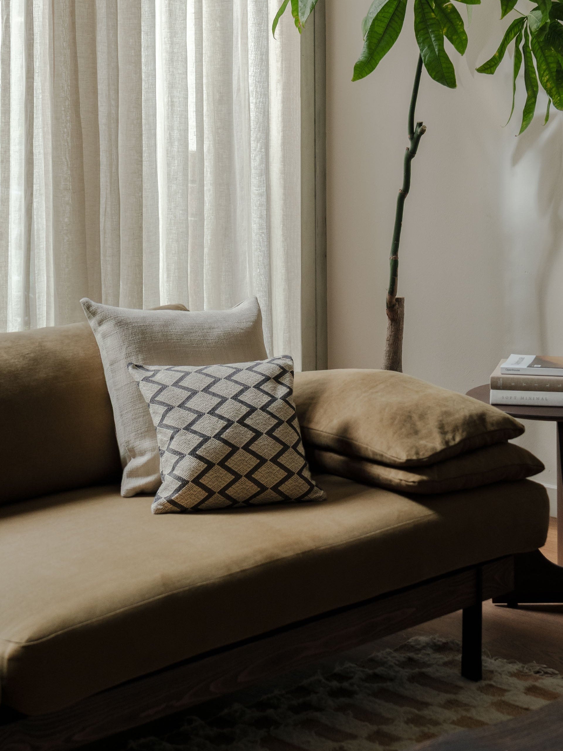 Fine Repeat – Small Pair styled on a dark sofa in a living room with a side table and plant