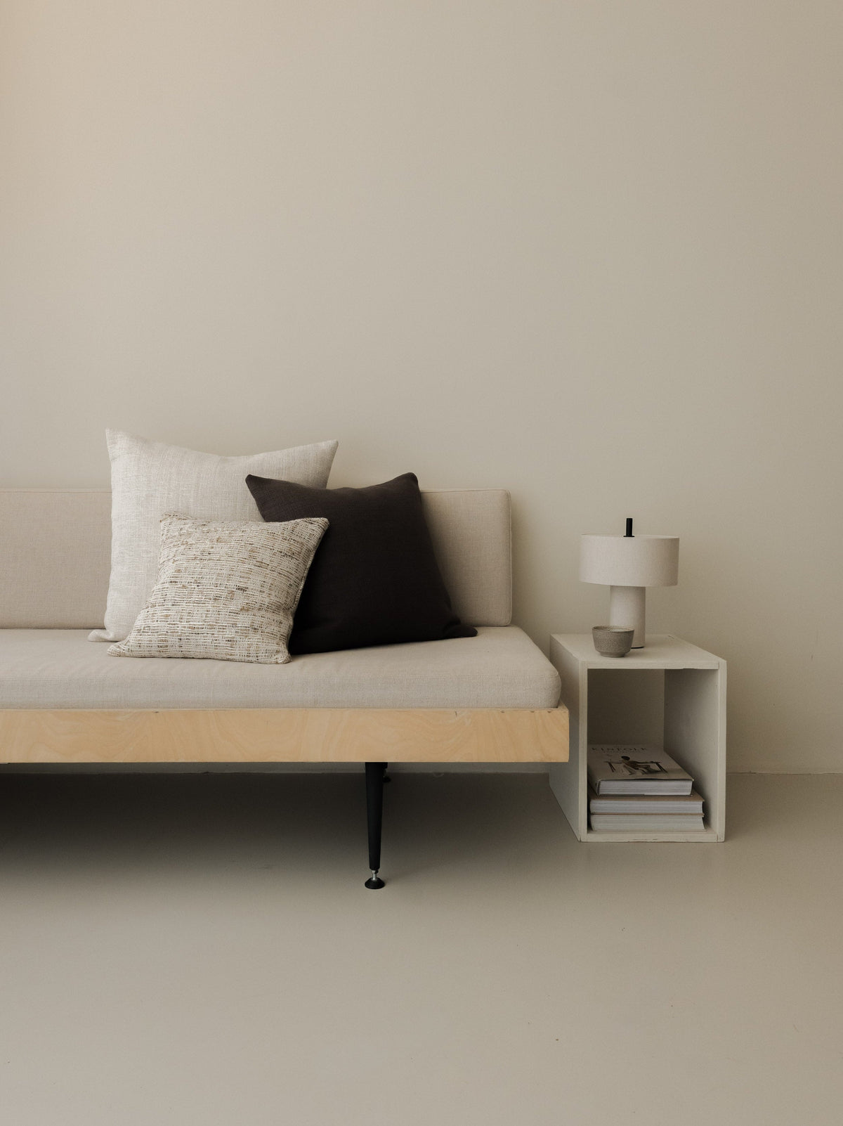 Raw Tones – The Square Trio, featuring three textured cushions in warm neutral shades, styled on a white sofa with a wooden frame