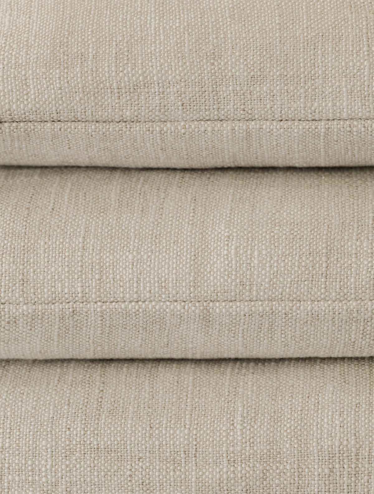 Close-up of a stack of three Mélange Moderne – Calcare cushions, highlighting the soft woven texture and subtle tonal variation