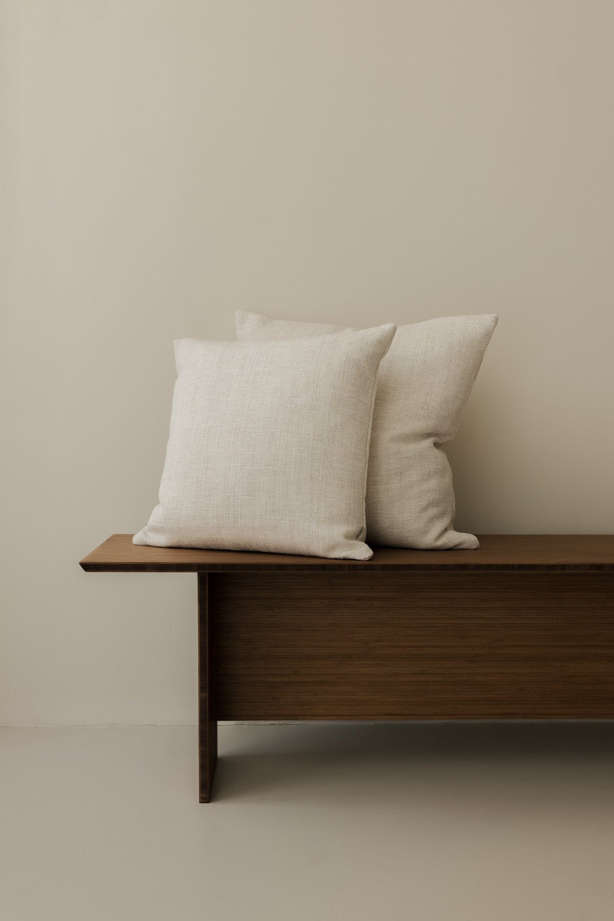 Mélange Moderne – Calcare cushions in 50 × 50 cm and 60 × 60 cm, displayed together on a dark wooden bench