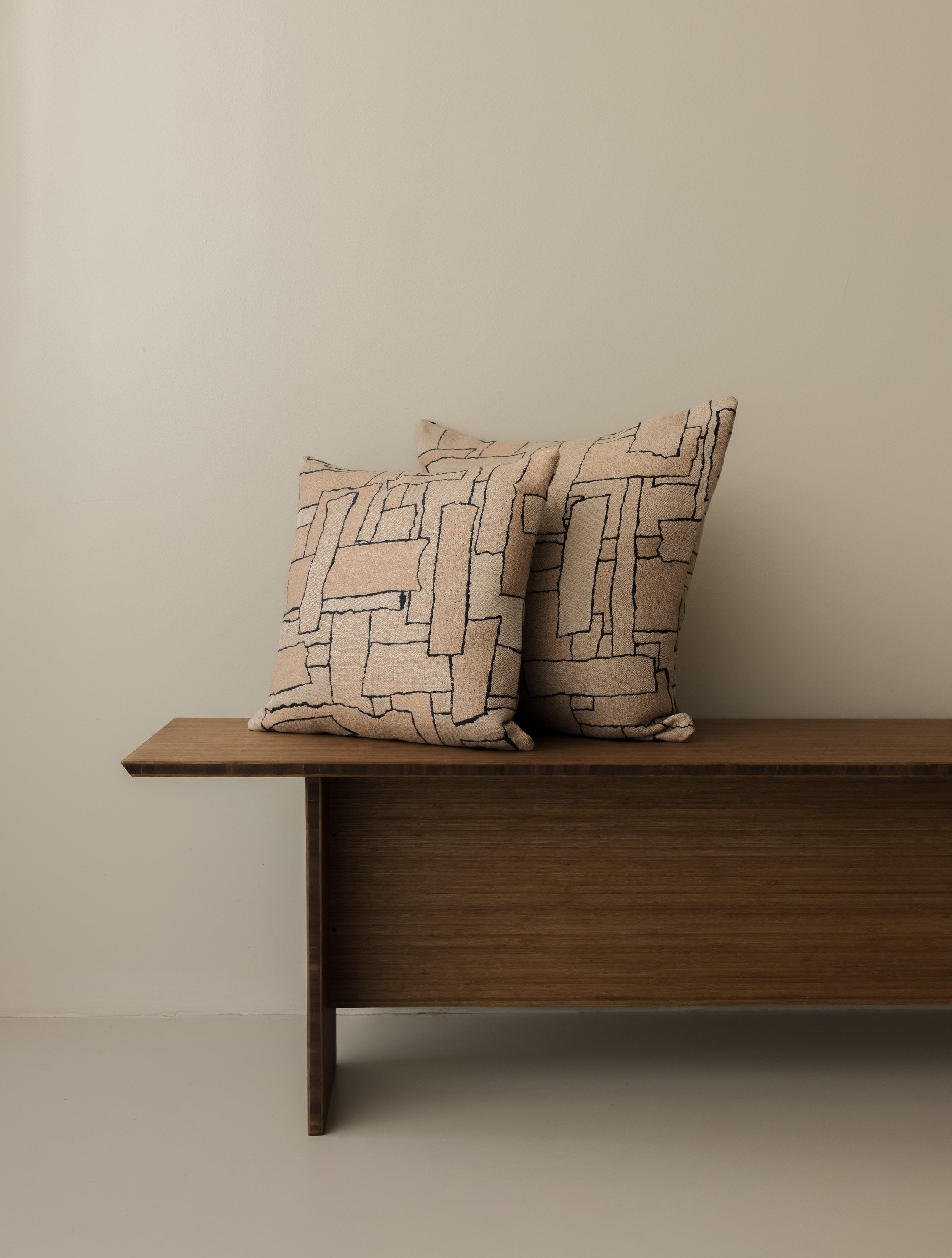 Naoki – Rose des Sables cushions in 40 × 40 cm and 50 × 50 cm, displayed together on a dark wooden bench