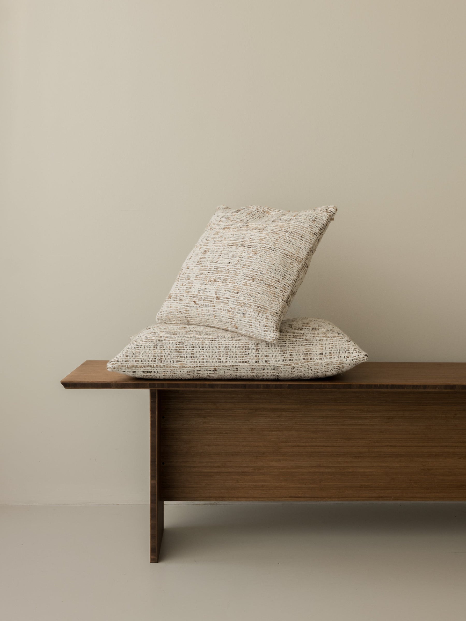 Coussins Nicomaco – Raw, formats 40 × 40 cm et 60 × 40 cm, présentés ensemble sur un banc en bois foncé