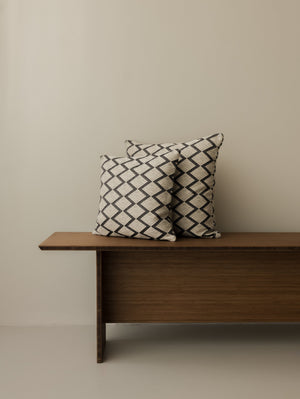 Coussins Papunya – Ombre Naturelle, formats 40 × 40 cm et 50 × 50 cm, présentés ensemble sur un banc en bois foncé