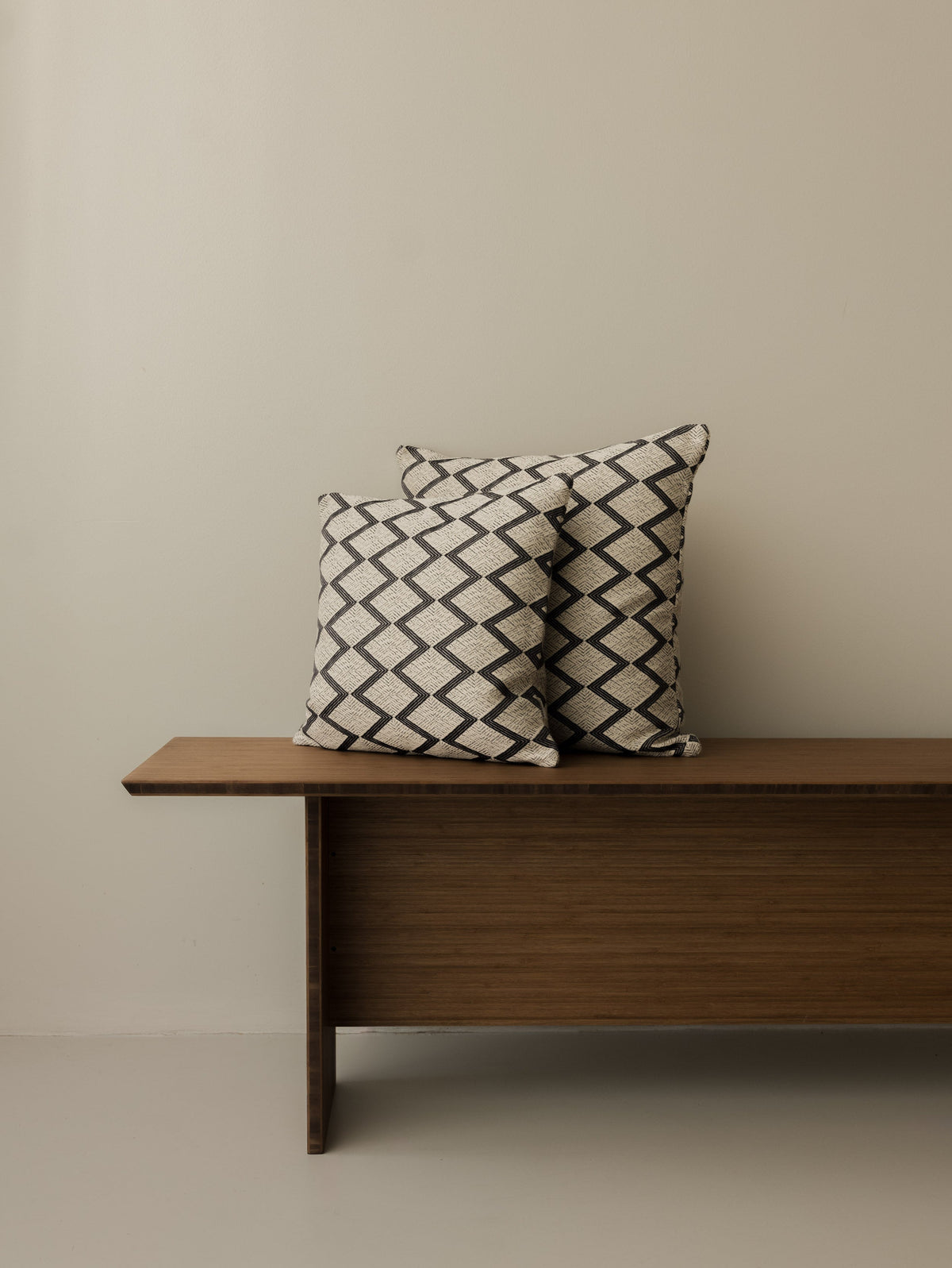 Coussins Papunya – Ombre Naturelle, formats 40 × 40 cm et 50 × 50 cm, présentés ensemble sur un banc en bois foncé
