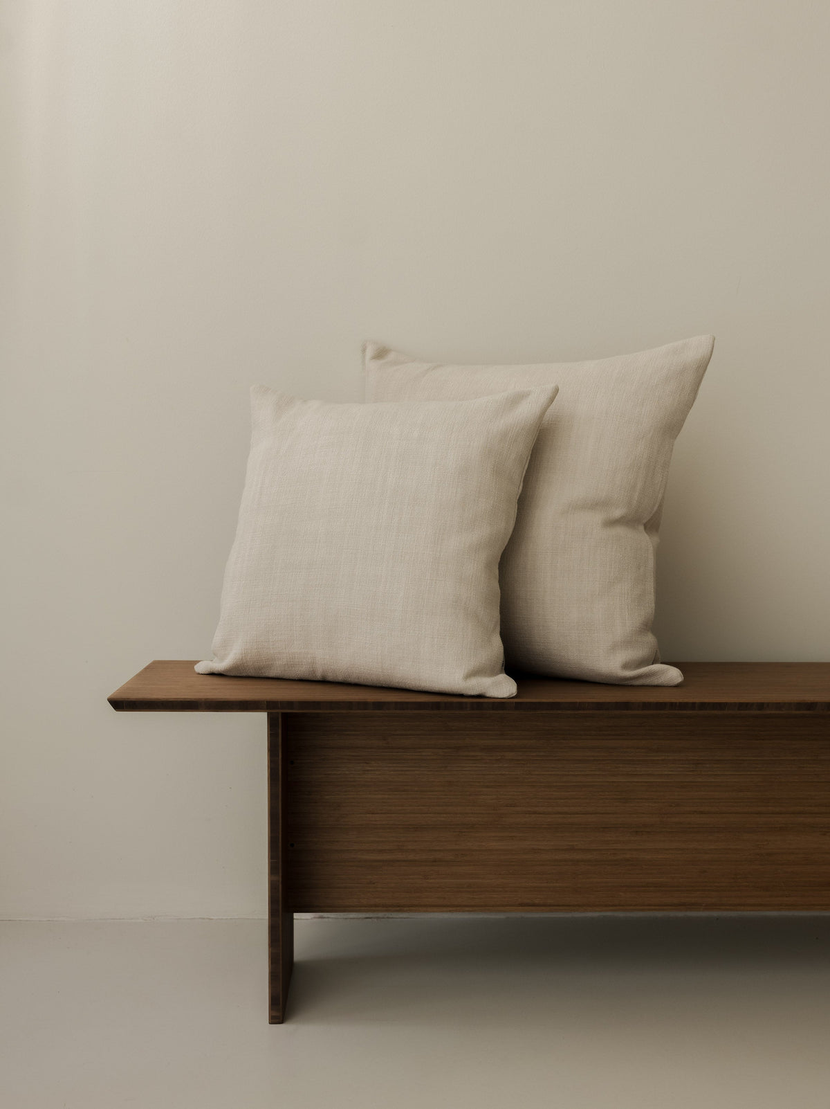 Paradou – Dune cushions in 50 × 50 cm and 60 × 60 cm, displayed together on a dark wooden bench