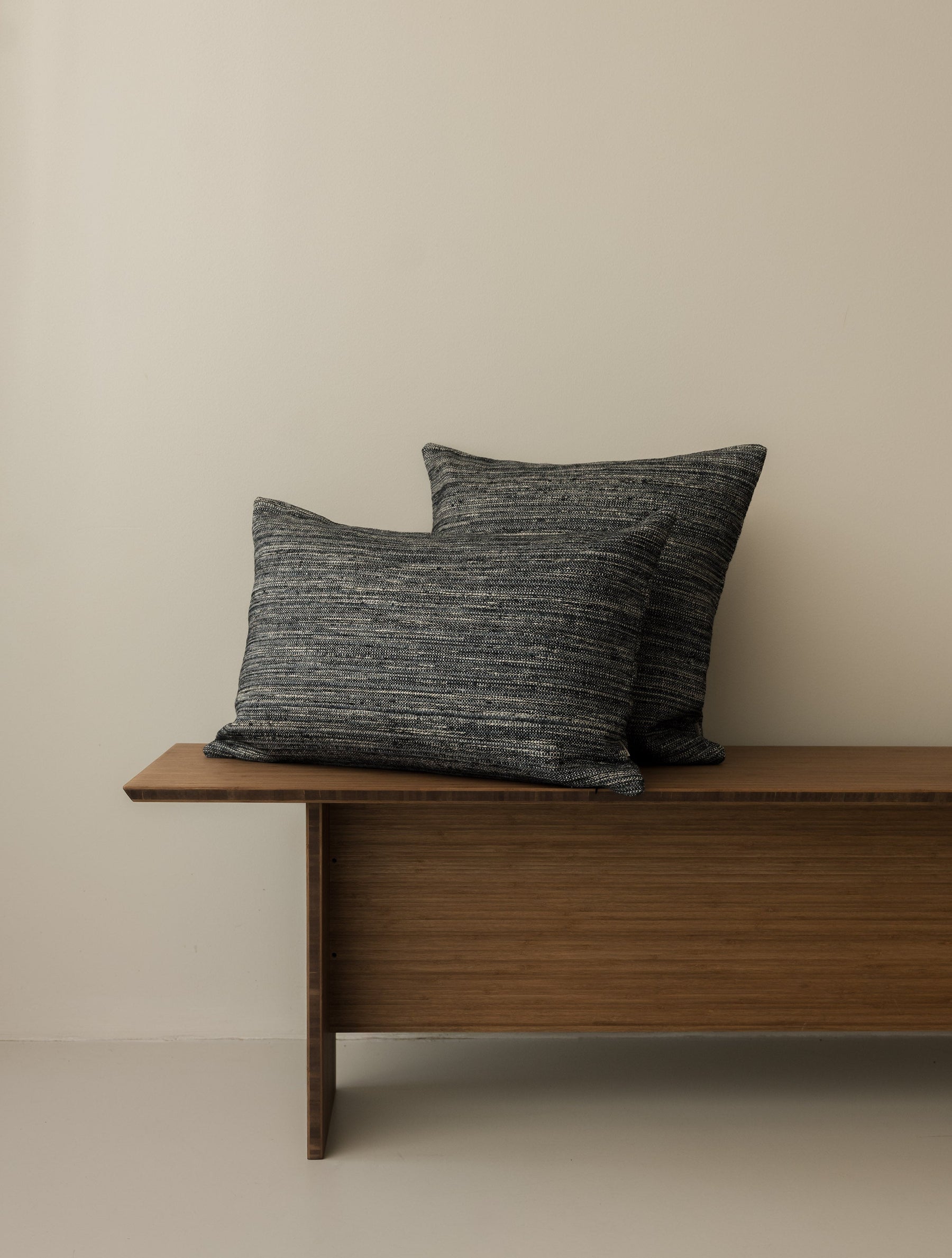 Roquebrune – Ebano cushions in 50 × 50 cm and 60 × 40 cm, displayed together on a dark wooden bench