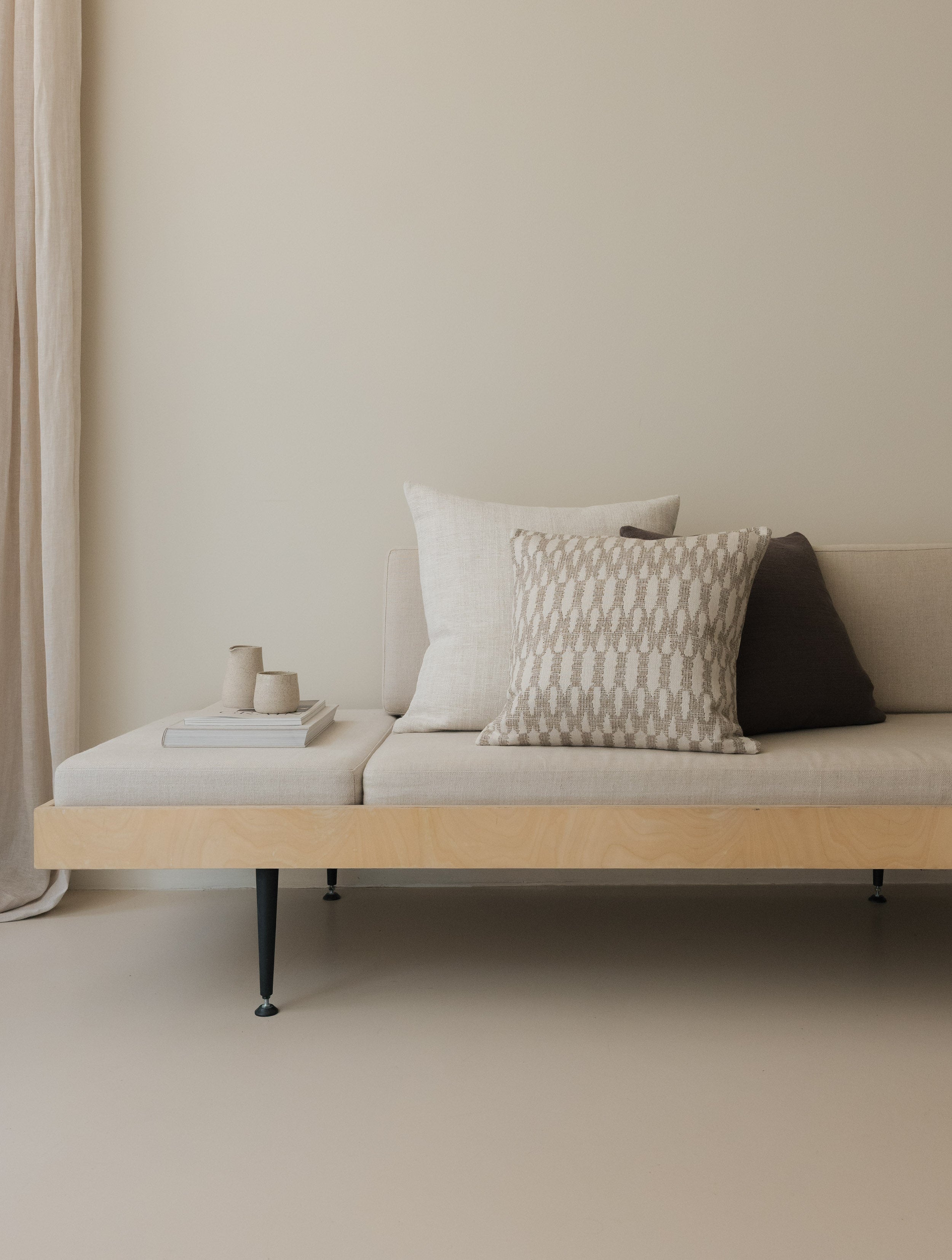 Shifting Shades – The Square Trio, featuring three textured cushions in layered neutral tones, styled on a white sofa with a wooden frame